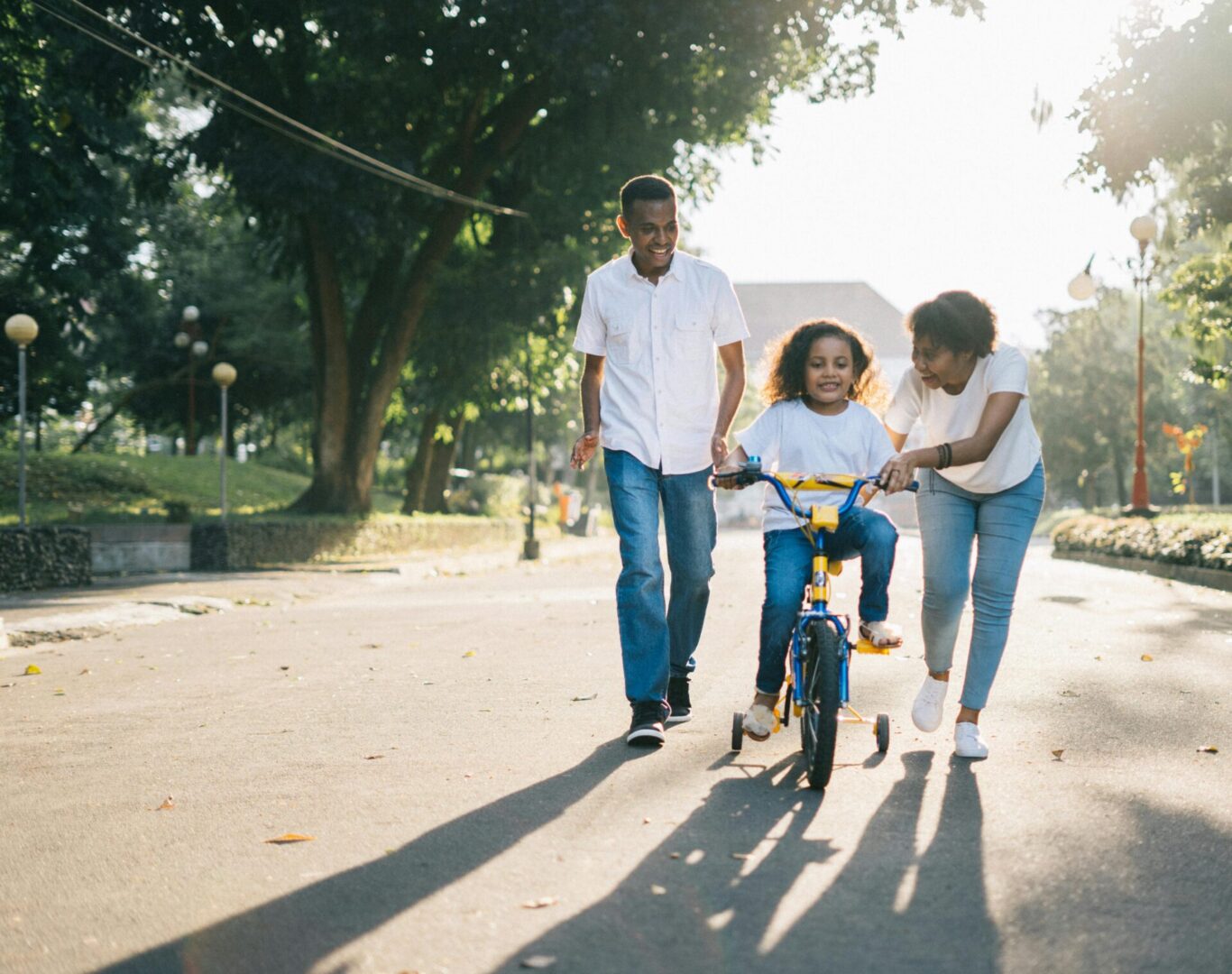 A young girl riding on the back of her bike while being pulled by an adult.